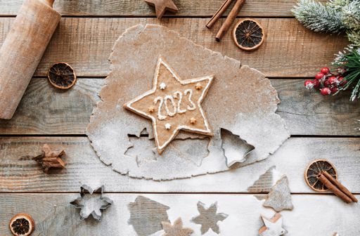 Flat lay photo of gingerbread cookie dough and winter holiday season decorations on rustic wooden table. Star shaped cookie with number 2023.