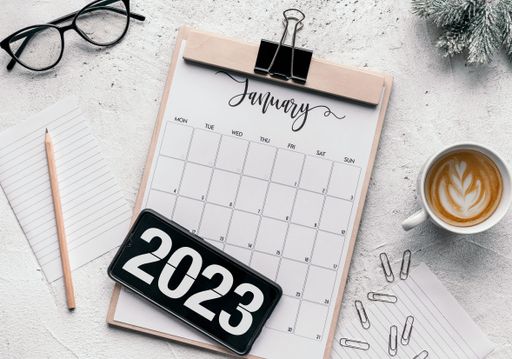 Top view of notepad with January 2023 calendar on table. Number 2023 on mobile phone screen.
