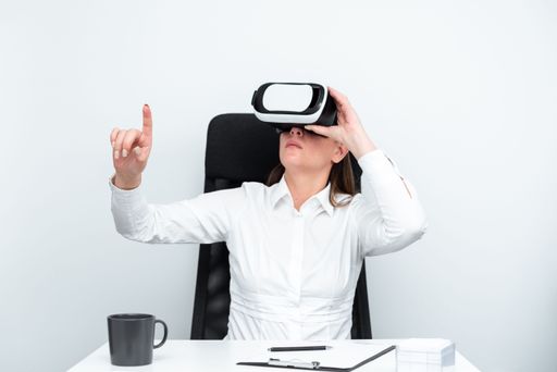 Businesswoman Wearing Virtual Reality Goggles And Learning Skill Through Futuristic Simulation. Woman Gesturing While Sitting At Desk During Training.