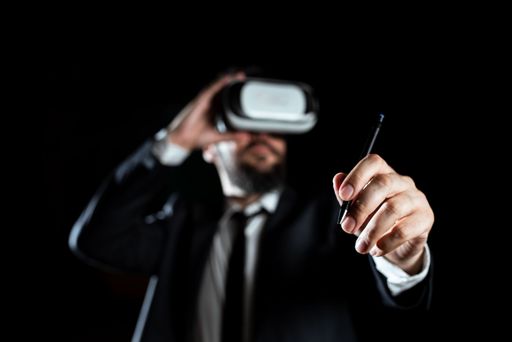 Male Wearing Virtual Reality Goggles Holding Pen And Presenting Technology Of Learning. Businessman Wearing Suit Training Through Simulator.