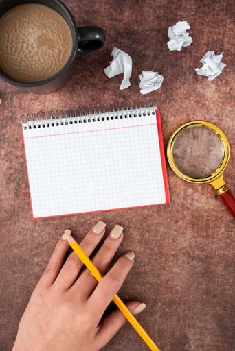 Hand Of Woman Having Spiral Notebook With Copy Space, Pencil, Coffee Cup And Crumpled Papers. Businesswoman Writing Message On Book.