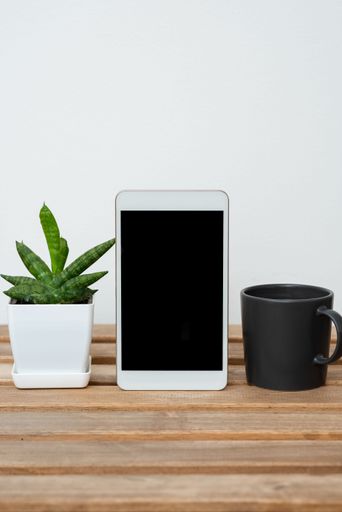 Tablet With Information On Table With Plant And Cup Of Coffee. Crutial Announcements Presented On Cellphone Screen On Desk With Flower And Mug.