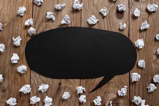 Speech Bubble On Floor With Information Written In With Paper Wraps Around. Dialogue Balloon On Ground With News Inside And Crumpled Notes All Over.