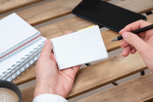 Businesswoman Holding Pen And Notepad With Message With Notebooks And Phone. Woman Presenting Information On Paper On Desk With Cellphone And Coffee