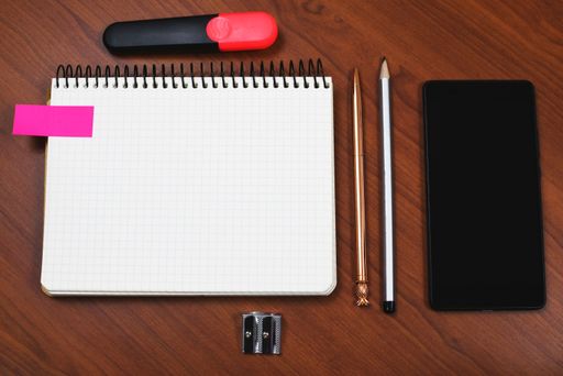 Notebook With Message On Desk With Pen, Pencil, Sharpener, Marker And Cellphone. Notepad With Crutial Information On Table With Mobile Phone.