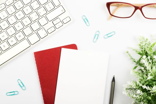 Announcements On Piece Of Paper Over Notepad On Desk With Flower, Glasses, Pen, Hot Drink And Keyboard. Ideas On Note Over Notebook With Pencil.