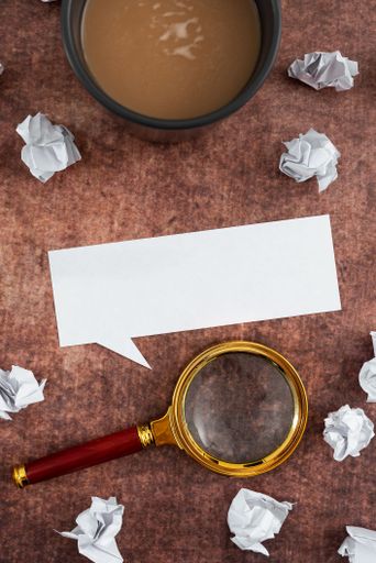 Speech Bubble Made Of Sheet With Magnifying Glass, Coffee Cup Surrounded With Crumpled Papers Over Wooden. It Is Presenting Analyzing Of Plans 