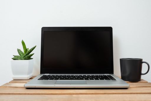 Lap Top With Information On Table With Plant And Cup Of Coffee. Crutial Announcements Presented On Computer Screen On Desk With Flower And Mug.