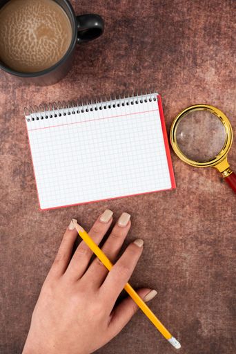 HOf Woman Having Spiral Notebook With Copy Space, Pencil, Magnifying Glass Coffee Cup Over Table. Businesswoman Writing Message On Book With Drink.