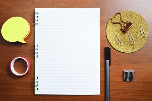 Notebook With Message On Desk With Pen, Sharpener, Notes, Paperclips And Tape. Notepad With Crutial Information On Table With Office Supplies.