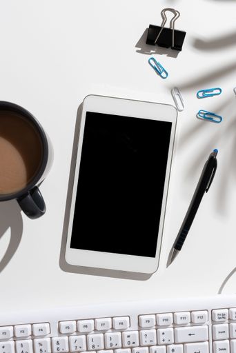 Phone Screen With Messages On Desk With Coffee, Pen, Paprclips And Keyboard. Information On Cellphone On Table With Cup. Late Updates Presented.