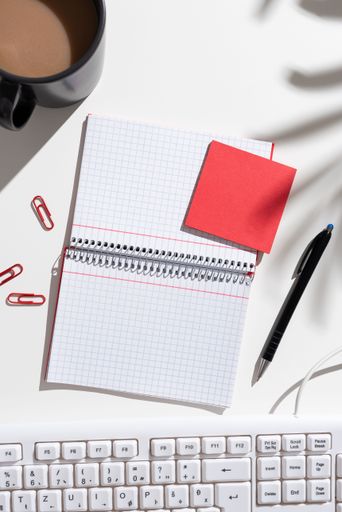 Notebook With Messages On Both Sides On Desk With Coffee, Pen, Paperclips, Keyboard And Memos. Information On Pad On Table With Cup And Pencil.