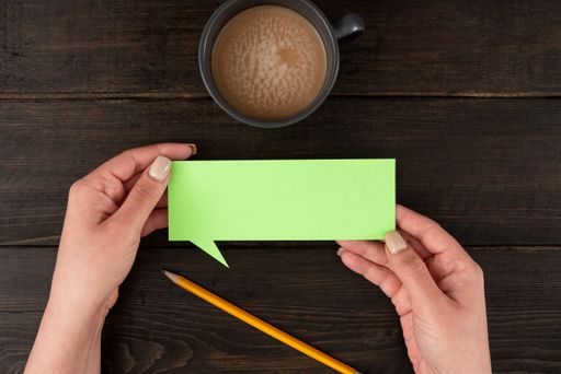 Hands Of Woman Having Thought Bubble Sheet With Cup Pencil Over Wooden Background. Businesswoman Holding Color Paper With Copy Space For Branding.