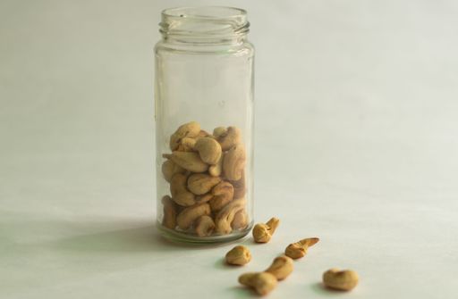 A glass jar with almonds and cashews with some out on white background