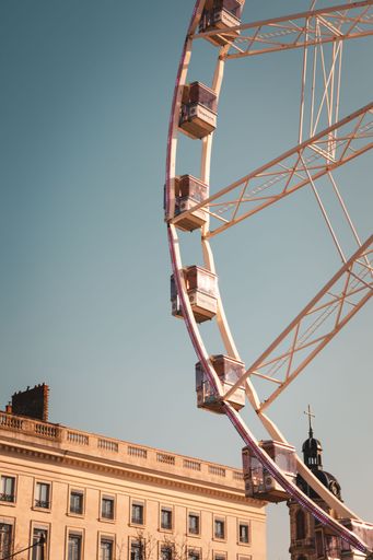 A vertical shot of the Ferris wheel against the background of the buildings and sky. Lyon, France.