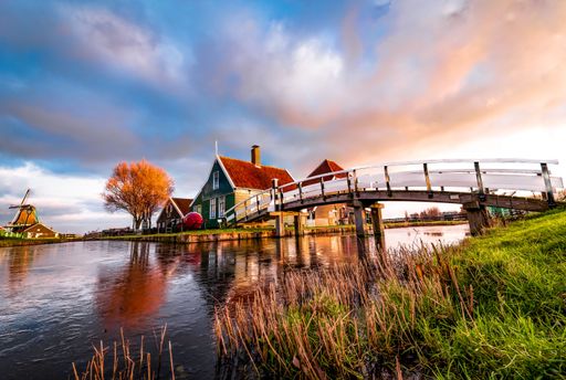 The bridge over the water with houses ad windmill reflected on the surface in Zaanse Schans, Holland