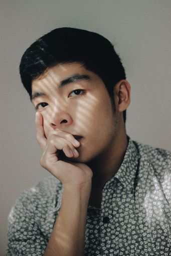 A vertical shot of Asian male thinking with his hand under the chin on white background