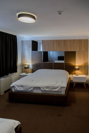 a vertical shot of a bedroom with a large white bed with lights turned on and curtains closed