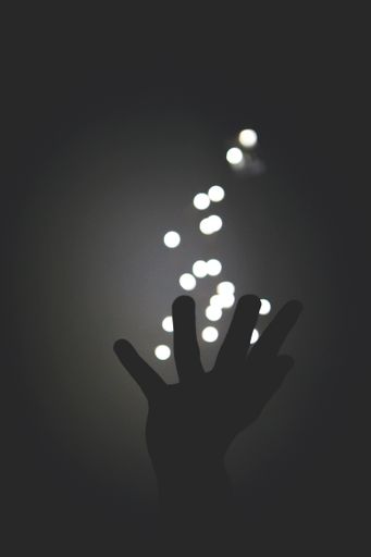A grayscale shot of bokeh lights coming out of the open hand of a person with a dark background