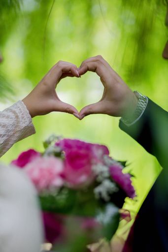 A vertical shot of a bride and a groom holding a heart with their hands