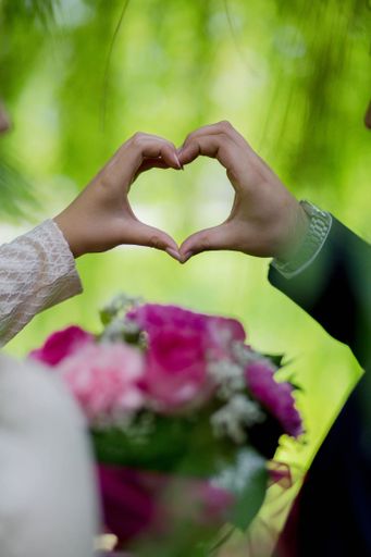 A vertical shot of the bride and the groom making a heart with their hands