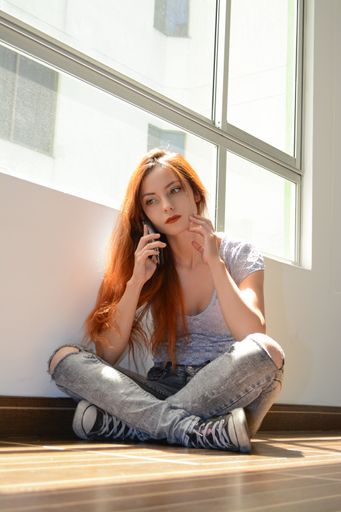 A vertical shot of a beautiful redhead lady using her phone sitting on the floor