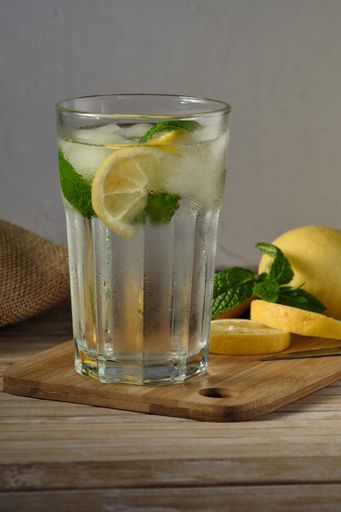 A vertical shot of a glass full of ice water, lemon, and mint on a wooden cutting board