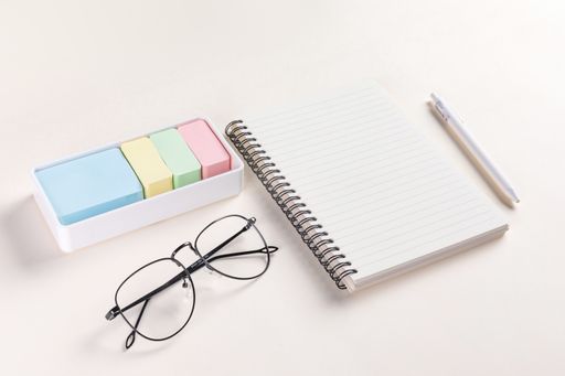A closeup shot of a notepad, a pen, glasses,  and sticky notes