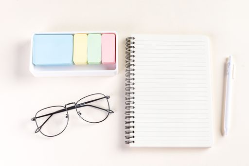 A closeup shot of a notepad, a pen, glasses, and sticky notes