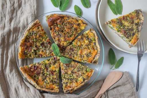 A closeup of a sliced quiche pie with spinach, cheese, and green peas.