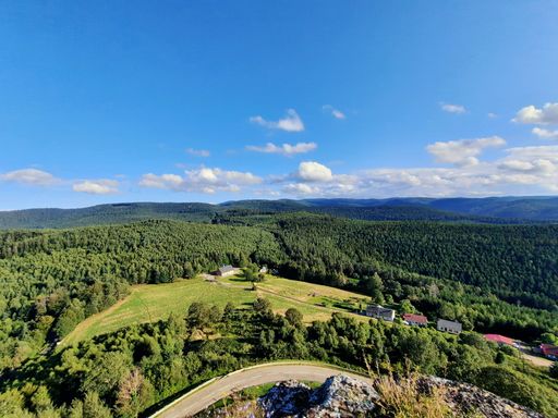 Stunning view of layered mountain ranges covered with dense forest, small village in green valley and road, under blue sunny sky