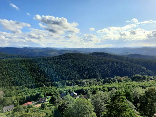 Stunning view of layered mountain ranges covered with dense pine forest and small village in green valley under blue cloudy sky