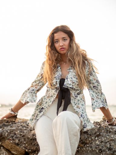A vertical shot of a pretty caucasian white girl sitting on the coastline rocks