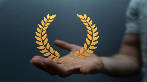 A hand with a gold laurel wreath symbol, isolated against a dark grey background