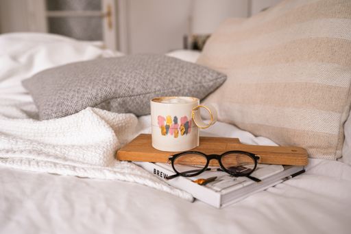 Beautiful cup of coffee set on a book and a pair of eye glasses on a cosy bed