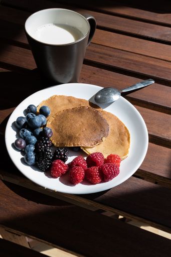 pancakes with cranberries and grapes on a plate with a cup of milk on a table. Healthy food