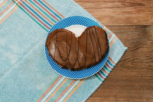 A top view of a chocolate covered pretzel, shaped like a heart, on a plate placed on a wooden surface