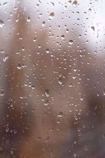 Textured surface of drops of autumn cold rain on window glass against blurred background of an empty dark city park. Rainy weather.