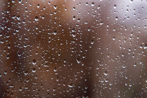 Textured surface of drops of autumn cold rain on window glass against blurred background of an empty dark city park. Rainy weather.