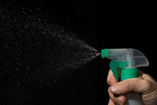 A hand squeezing a bottle of water spray on a black background