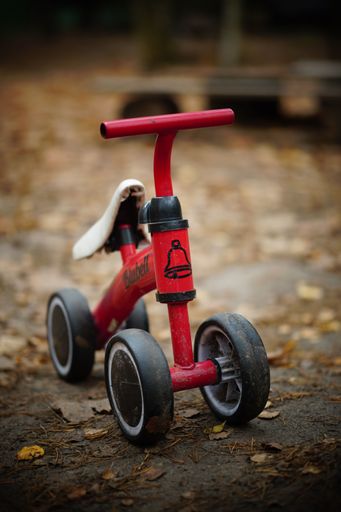 A vertical shot of Blubell brand red running bike for kids parked outdoors at fall