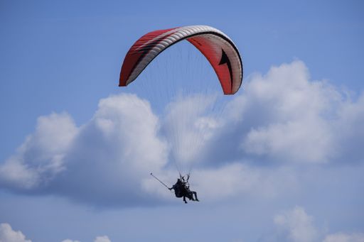An aerial shot of a paraglider high in sky with some clouds