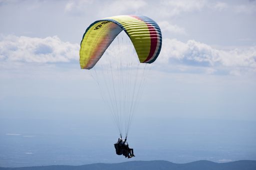 An aerial shot of a paraglider high in sky with some clouds