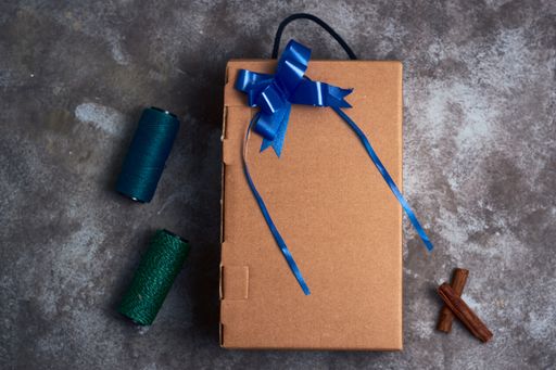 A top view of a Christmas present with blue and green threads, and cinnamon sticks next to it on a gray surface