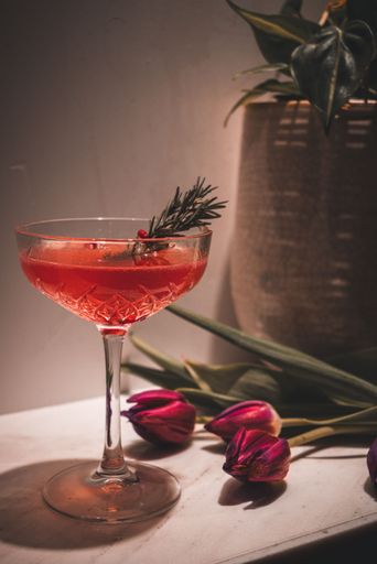 A closeup of a red cocktail with a beautiful garnish next to the tulips