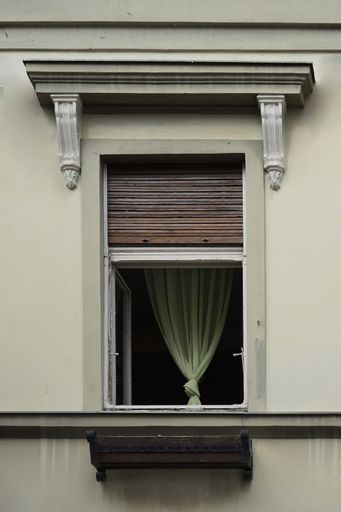 A vertical shot of an open window with a green curtain inside and an open shutter