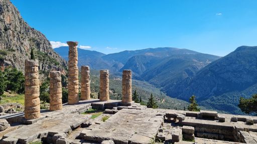 A scenic shot of the Temple of Apollo in Delphi, with a mountain range in the background