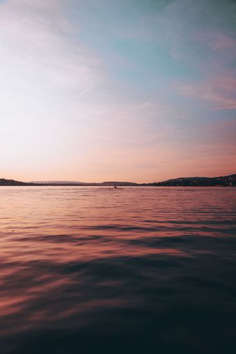 A vertical shot of a calm ocean with a mountain range in the background during an orange sunset