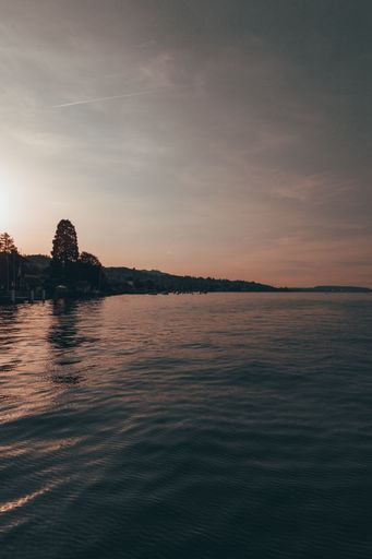 A vertical shot of a calm ocean with a mountain range in the background during an orange sunset