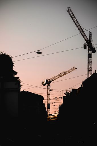 A vertical low angle shot of canes on a construction site during sunset